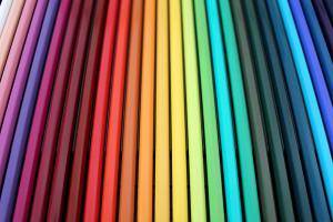 Viele farblich sortierte Buntstifte liegen nebeneinander aufgereiht.