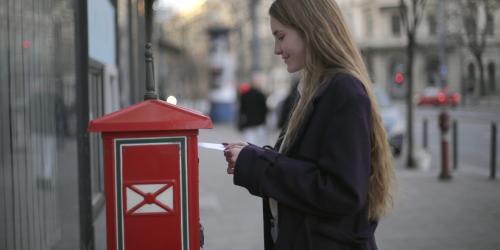 Frau mit Brief an einem Briefkasten